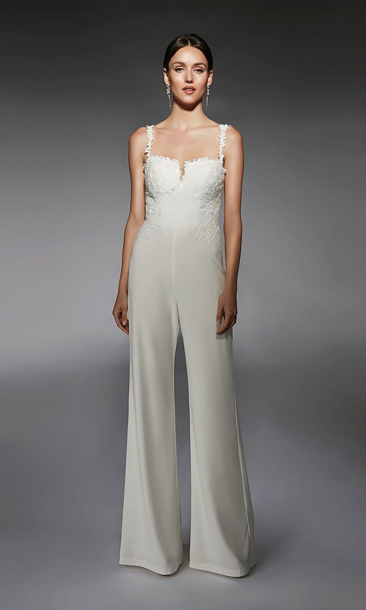 A woman faces forward, wearing the Long Formal Jumpsuit: Alyce 70073 in Diamond White with lace and floral embroidery on the bodice, set against a plain gray background.